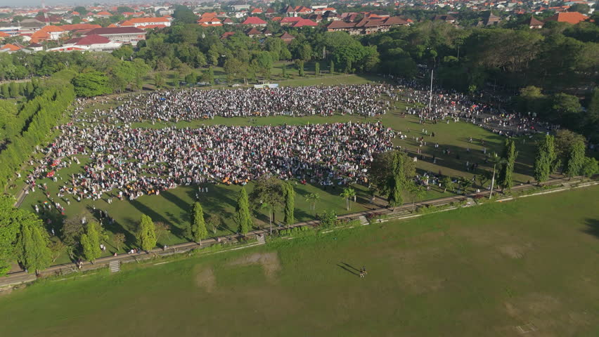 Eid al-Adha Morning Prayer Bali.
Aerial view of a large gathering of Muslim people for morning Eid al-Adha prayer in an open, grassy area in Bali.