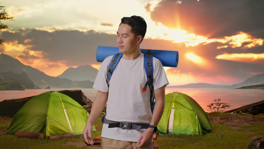 Asian Male Hiker With Mountaineering Backpack Smiling And Pointing To Side while Tent Camp Lakeside