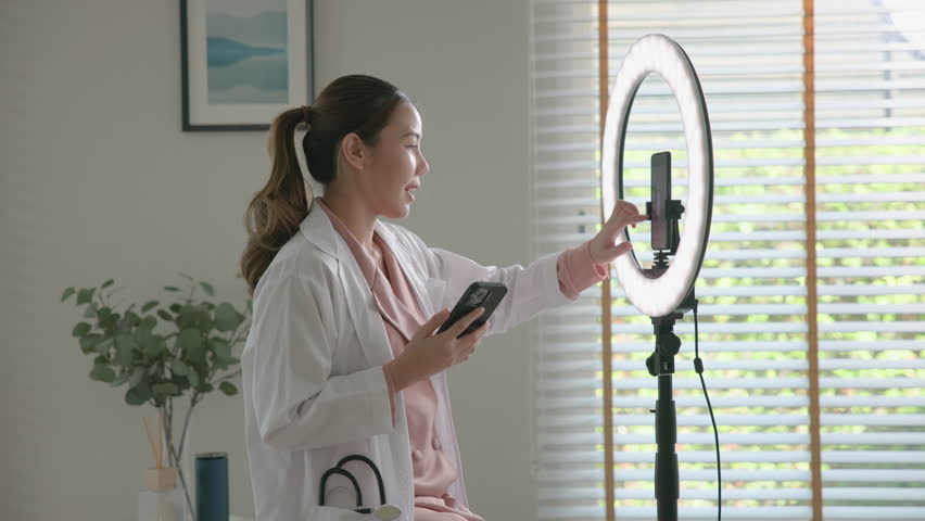 Young adult woman Gen Z asia people anti aging expert modern nurse live talk viral video selfie camera on mobile phone app mental health care. Online sharing digital virtual asian vlogger filming.