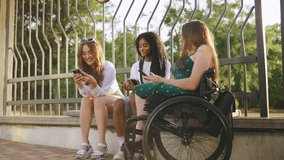 three multiracial female friends one disabled in a wheelchair enjoy a sunny day outdoors while using their smartphones in a park setting - Powered by Shutterstock - Get 15% off with code: PIKWIZARD15
