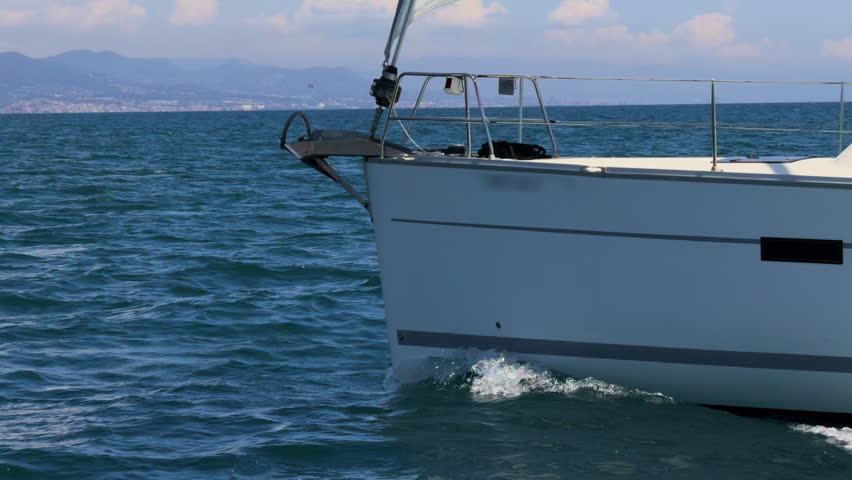 A sailboat glides through calm sea under a blue sky, creating a serene and peaceful nautical scene.