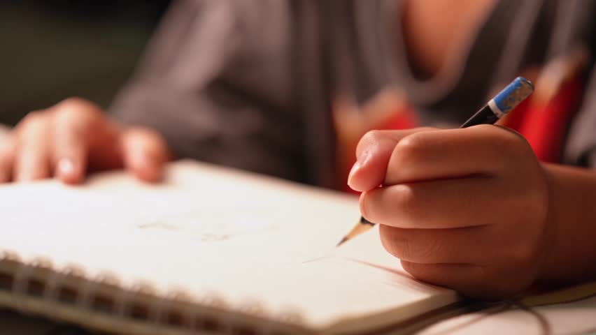 Close up of cute asian girl hand holding pencil drawing on white paper at home.