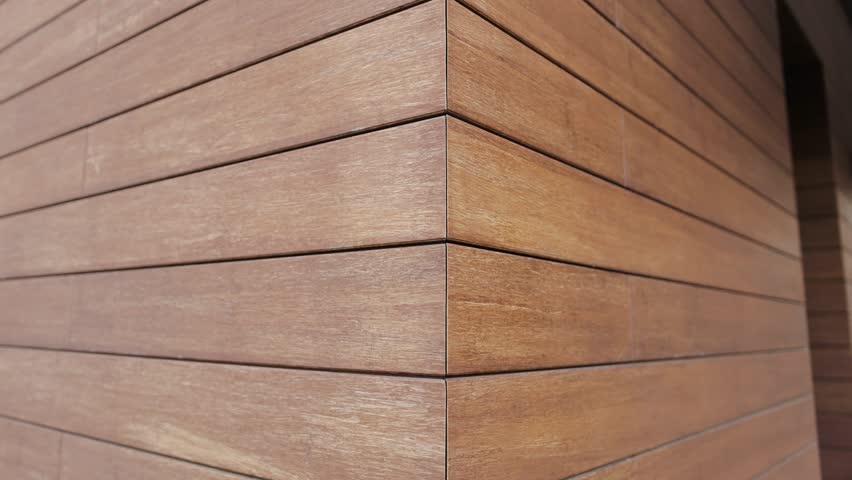 The camera moves in close-up along the wall of a house covered with tiles on the facade that imitate wood. Brick texture. House from the outside.