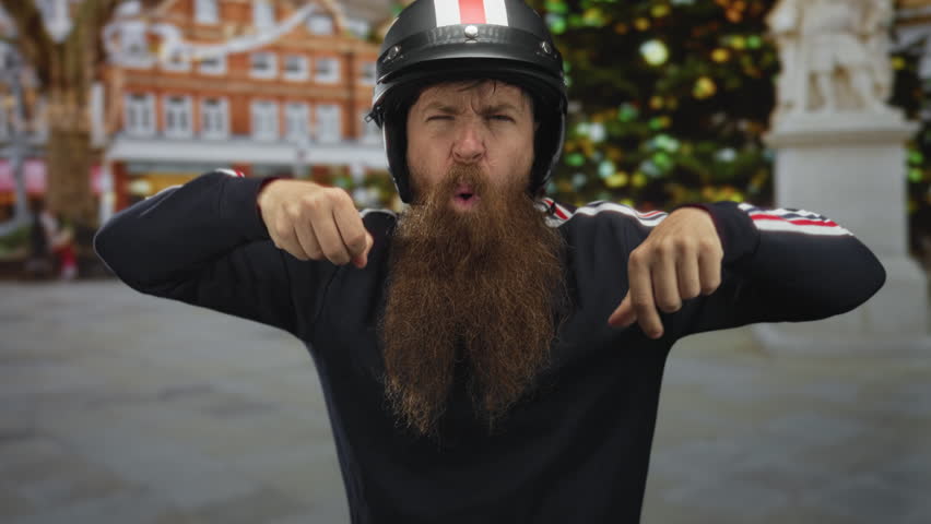 Helmeted bearded man mimes gripping handlebars in motorcycle riding gesture on street with blurred city buildings; adventure.