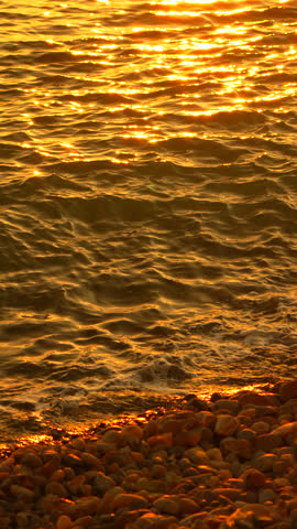 Sunset, Ocean, Water Beautiful golden sunlight glistens on rippling sea, with pebble beach and distant island. Vertical video.