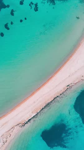 A vertical top down aerial view of a white sandy beach and turquoise waters on Sardinia coast, Italy glowing on a sunny day