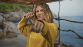 Woman covers one eye with a victory sign against a seaside backdrop by a blonde young model wearing a yellow sweater in portrait casual style. - Powered by Shutterstock - Get 15% off with code: PIKWIZARD15