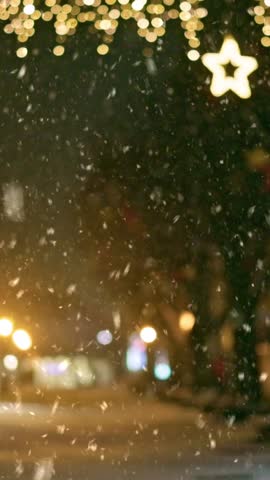 Vertical shot. Christmas city lights illuminate snowy winter streets as festive atmosphere fills the air. Cozy atmosphere of winter city decorated with Christmas decorations and lights