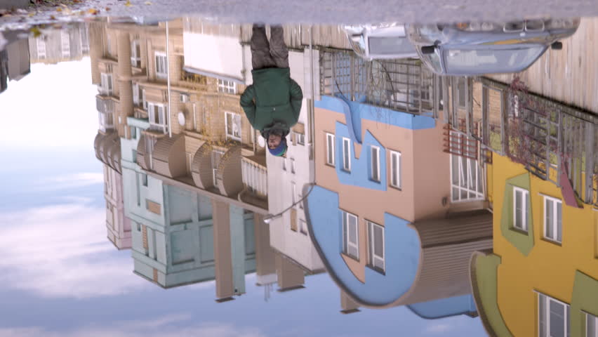 
reflection of a puddle. a European man walks down the street in warm clothes with a phone in his hands. autumn. 4k general plan
