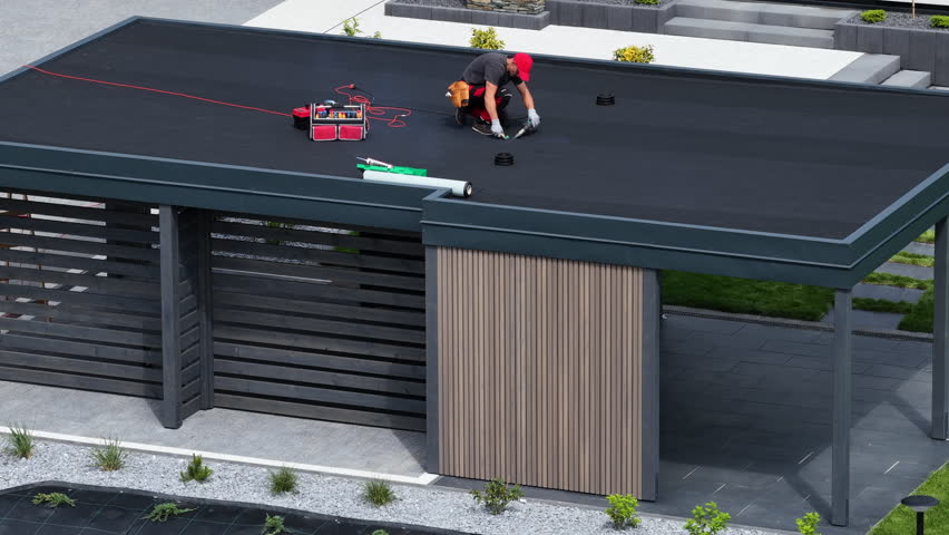 A professional contractor works on the flat roof of a contemporary structure, ensuring proper maintenance and upkeep while using various tools and equipment.