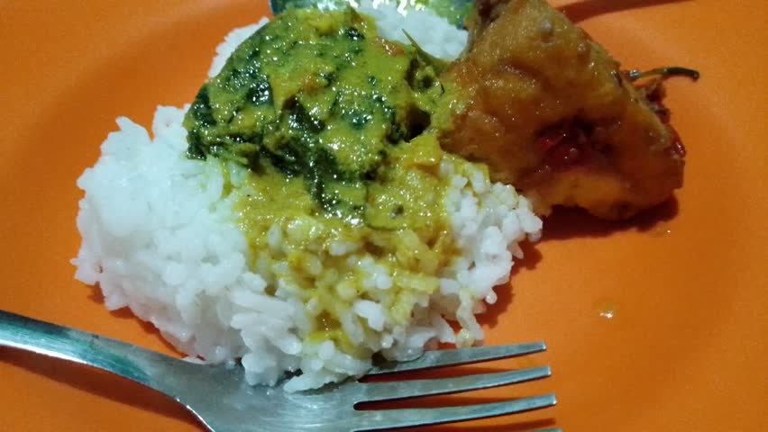 Rice with fish slices in coconut milk sauce, fried tofu, and chili sauce on an orange plate with a spoon and fork on opposite sides. Depok Indonesia July 20, 2025