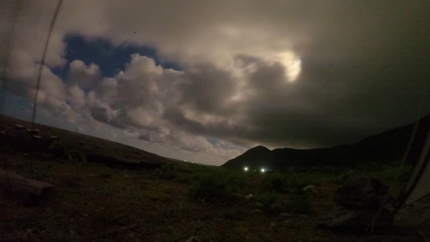 Time lapse of moon light with dramatic clouds movement in various shape fast speed at night by the rocky beach coastline look out to ocean horizon with forest and mountain from ground looking up sky