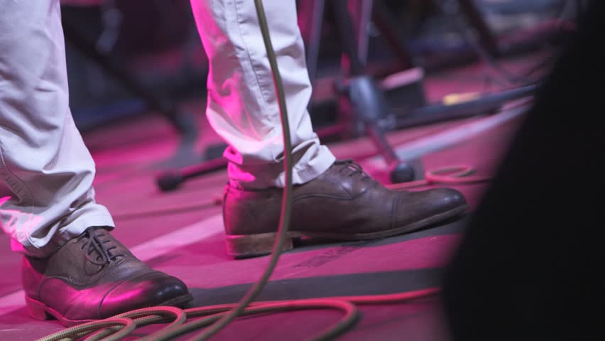 Leather clad musician's feet keeping steady rhythmic beat during energetic live performance, capturing raw musical passion from stage perspective