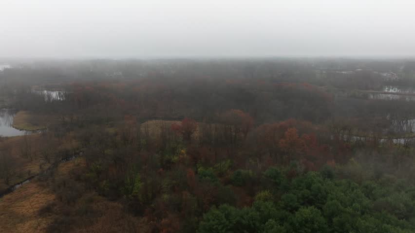 Aerial footage of forested land near Jackson Michigan on a foggy day in late autumn. The grand river snaking through colorful trees