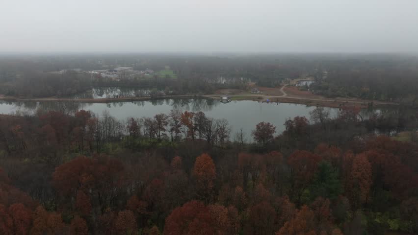 Aerial footage of forested land near Jackson Michigan on a foggy day in late autumn. The grand river snaking through colorful trees