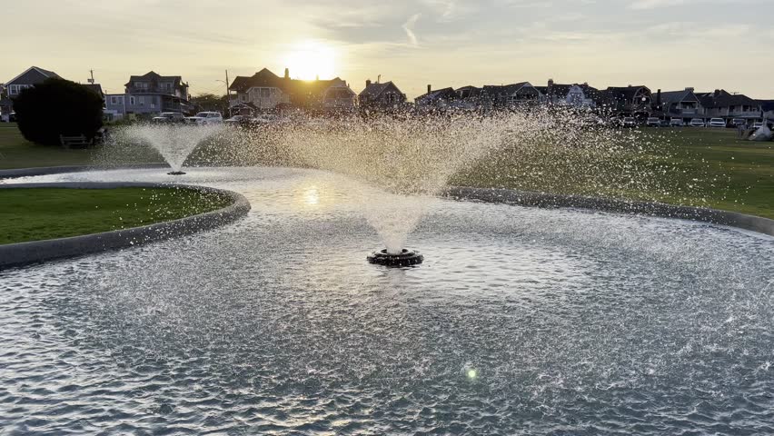 July 4, 2025 – Oak Bluffs, Massachusetts, United States – A public park at sunset on Independence Day in Oak Bluffs, Martha’s Vineyard. Silhouetted suburban homes line the horizon behind glowing water