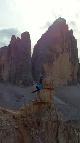 Vertical aerial view of the beautiful Tre Cime di Lavaredo peaks. A man and a woman admire the breathtaking views of the surrounding landscape and the mountain range in South Tyrol, Dolomites, Italy.