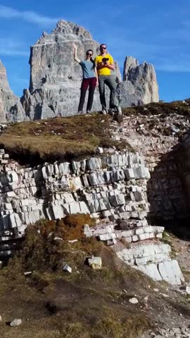 Vertical aerial view of the beautiful Tre Cime di Lavaredo peaks. A man and a woman admire the breathtaking views of the surrounding landscape and the mountain range in South Tyrol, Dolomites, Italy.