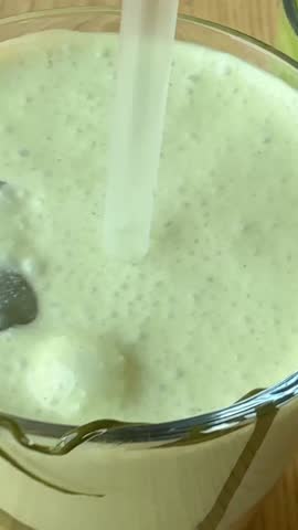 Preparation of summer refreshing beverage iced matcha latte, pouring matcha green tea mix into a glass of fresh full cream milk, cinematic close up shot.