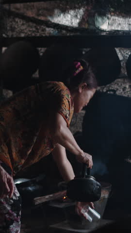 Vertical clip of Rural kitchen setting with elderly women preparing tea on a wood fire