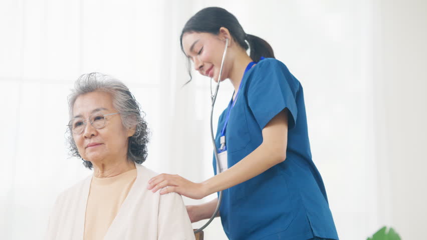 Asian woman doctor examine senior patient use stethoscope listening to the sounds of heart and lungs on the bed. Nurse visit and checking elderly woman health at home. Home medical therapy concept.