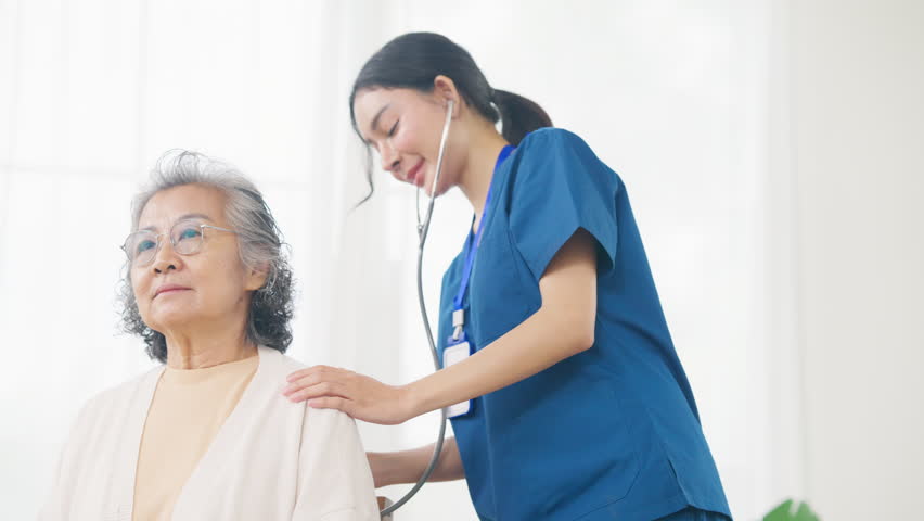 Asian woman doctor examine senior patient use stethoscope listening to the sounds of heart and lungs on the bed. Nurse visit and checking elderly woman health at home. Home medical therapy concept.