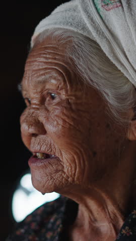 Vertical clip of Old woman with few teeth chews fresh strawberries with difficulty in humble surroundings