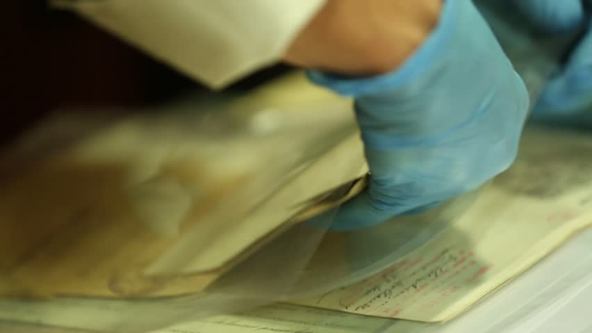 Gloved hands carefully examine old, fragile historical documents and newspaper clippings. Archiving and preserving vintage papers for research, history, and knowledge.