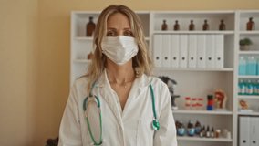 Young blonde woman doctor in a clinic room with stethoscope adjusting face mask indoors with medical equipment visible in background suggesting professional healthcare environment - Powered by Shutterstock - Get 15% off with code: PIKWIZARD15