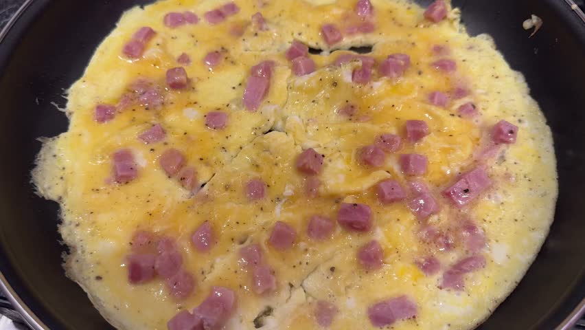 A ham and cheese omelette cooking in a frying pan