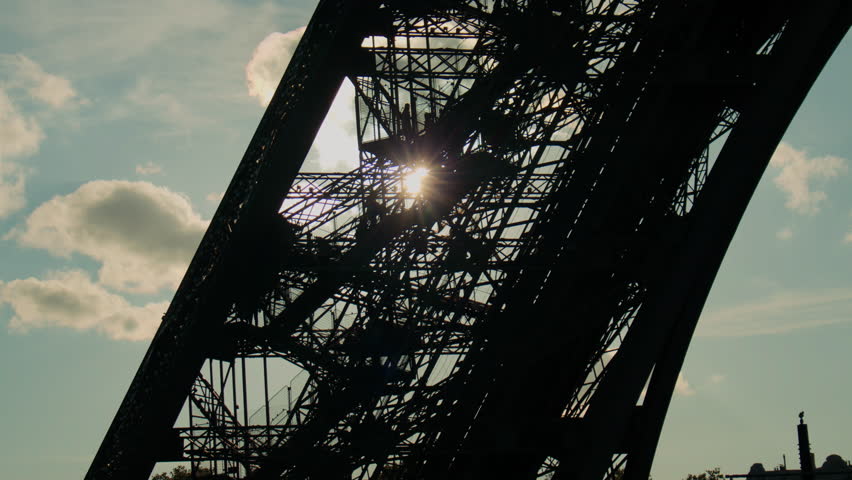 Eiffel Tower stair silhouette at sunset, with people, sun rays, and dramatic sky. Silhouettes of people walking on the Eiffel Tower's stairs during sunset, with sun shining through the iron lattice