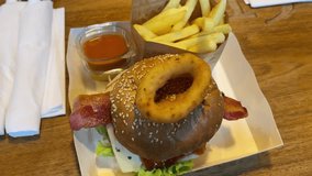Close-up of delicious bacon cheeseburger with onion ring on sesame bun, served with crispy French fries and dipping sauce on wooden table - Powered by Shutterstock - Get 15% off with code: PIKWIZARD15