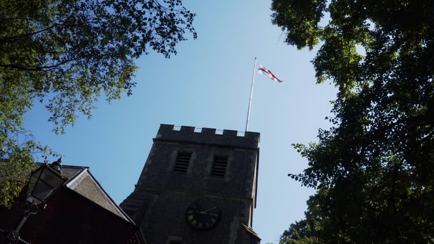 England Flag Waving Against Clear Blue Sky Atop Historic Church


