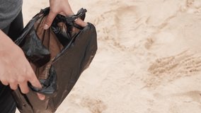 Top view of a volunteer's hands putting a plastic bottle into a black trash bag during a beach cleanup. This shows environmental activism, recycling to fight plastic pollution and protect our oceans. - Powered by Shutterstock - Get 15% off with code: PIKWIZARD15