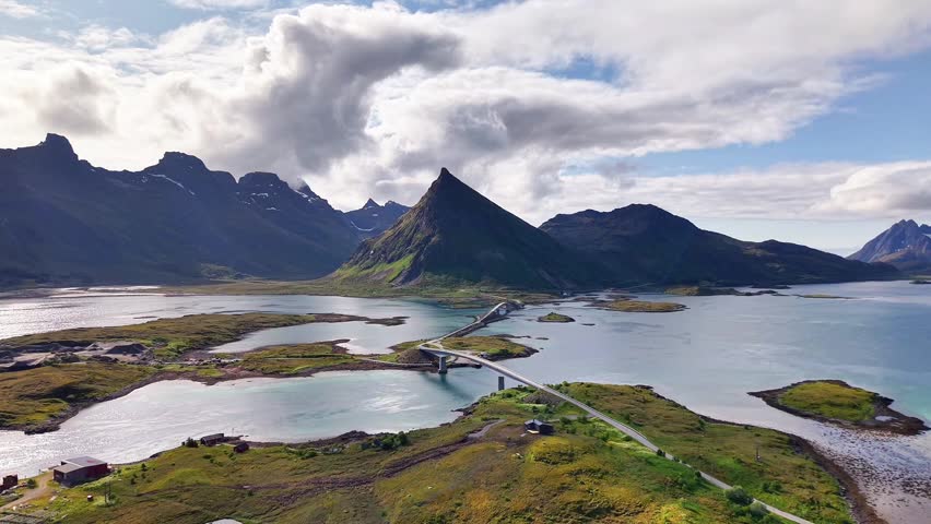 Aerial view of a sharp, pyramid-shaped mountain with a scenic bridge and coastal landscape in Norway. Captured by drone on a summer day.