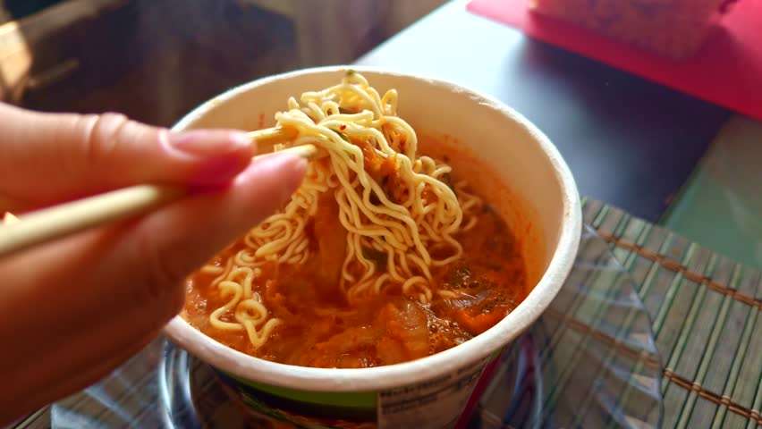 Hot and spicy instant noodles being lifted from paper cup lunch. Portable food Asian cuisine for dinner. Ready-to-eat ramen. Unami flavor instant noodles. Asian food.  Fast food dinner meal noodles 
