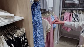 Woman shopping in stylish clothing store, browsing through rack colorful summer dresses. Modern fashion retail with displayed garments, light tones casual outfit choices, shopping experience boutique - Powered by Shutterstock - Get 15% off with code: PIKWIZARD15
