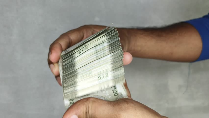 Extreme close up of hand showing and flipping stack of 500 rupees Indian currency notes. Budget, savings, black money, profit, illegal income, wealth, success, corruption and bribery concept.