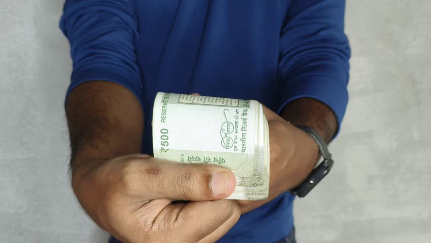 Close up of hand holding showing and flipping stack of 500 rupees Indian currency notes. Budget, savings, black money, profit, illegal income, wealth, success, corruption and bribery concept.
