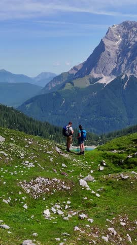 Vertical aerial drone view of the Alps and the green Seebensee  on a sunny summer day. A couple enjoys the view of Seebensee and goes hiking.