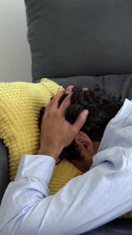 Depressed man lying on the sofa and holding his head. Sad unhappy handsome caucasian man on couch having financial troubles during quarantine or suffering from loneliness.