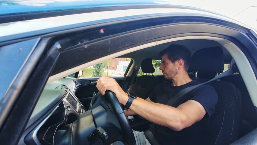 Male driver maneuvering car during parking, turning steering wheel and looking in mirrors. Person drives car, moves in reverse