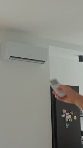 Close-up of hand using remote control to adjust temperature on wall-mounted air conditioner. Concept of indoor climate control and cooling during hot weather
