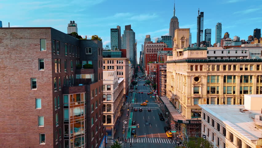 Following multiple yellow cabs in the traffic by the Fifth Avenue. Drone footage along the facades of the buildings in New York City.