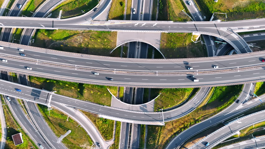 Descending above the complicated road system. Cars move quickly by the conjunction with highways and freeways. Top view.
