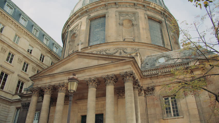 Grand neoclassical church in Paris, with Corinthian colaumns, ornate detailing, domed roof, and aged stone facade under partly cloudy sky. Low angle view of Notre-Dame-de-l