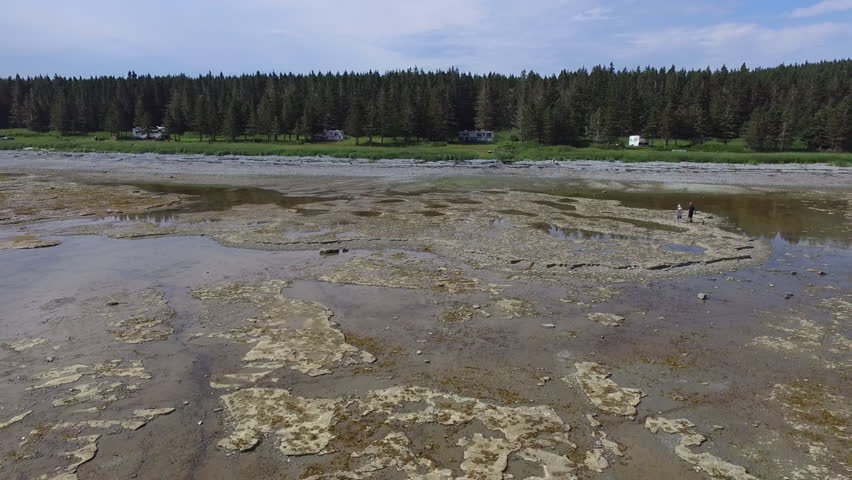 Two People Walk Along the Dry and Rocky Parts of the River Shore next to the Forest, at  Trois Ruisseaux Bays, in Anticosti, Quebec, Canada 