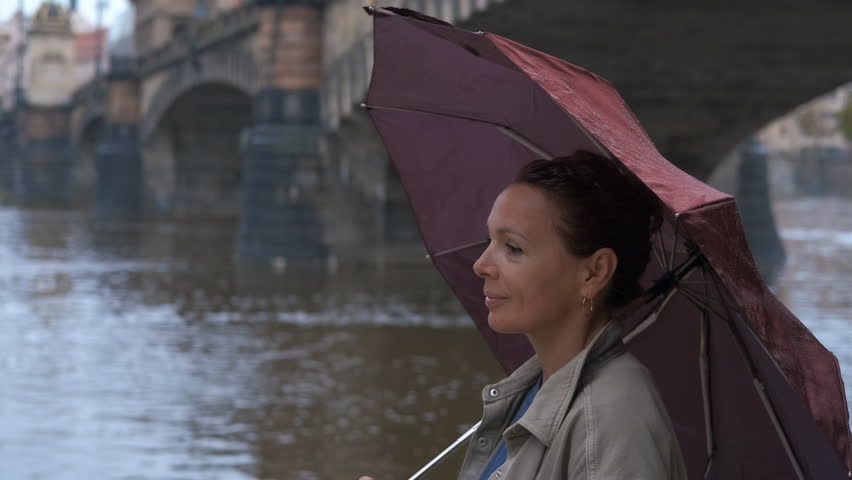 Woman with umbrella near the river and the Legion Bridge in Prague. Tourist woman standing under umbrella, gazing across river beside legion bridge, capturing urban scenery in prague