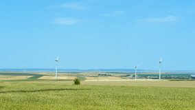 Environmentally friendly renewable energy. Wind turbine is rotating in a wheat field on a sunny day. The camera is panning to the right, showing the vastness of the field and the blue sky - Powered by Shutterstock - Get 15% off with code: PIKWIZARD15