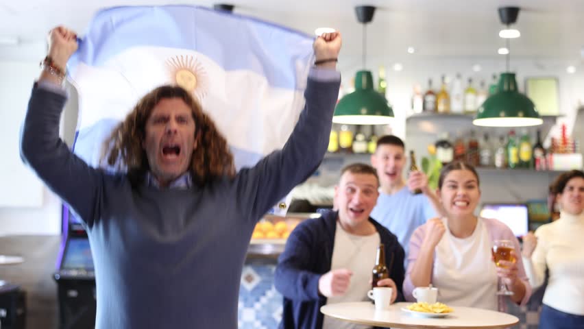 Happy international sport fans waving the flag of Argentina and drinking beer, watching football match in the bar. High quality 4k footage